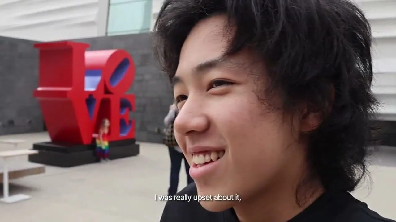 A frame from the rough cut, with a person smiling in front of a red LOVE sculpture.